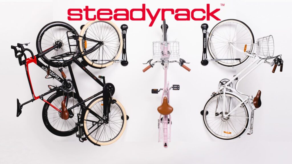 Steadyrack brand promotional image showing three different bicycles mounted vertically on Steadyrack wall-mounted bike storage racks with the red Steadyrack company logo, representing innovative space-saving bike storage solutions
